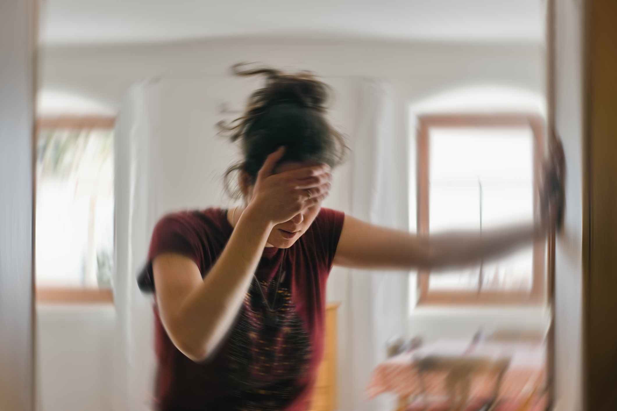 Frau hat einen Migräneanfall und hält sich am Türrahmen fest
