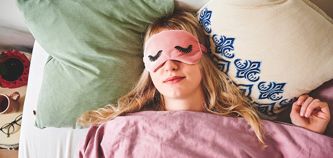 Frau schläft in Bett und trägt eine Schlafmaske