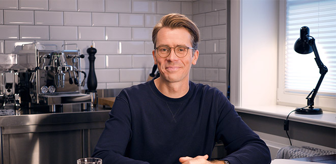 Dr. Johannes Wimmer sitzt in einer Küche und guckt in die Kamera